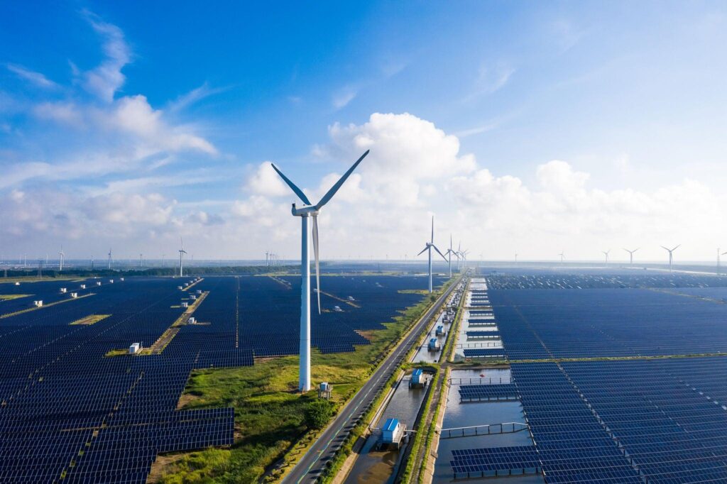 Mehrere Windkraftanlagen und große Solarfelder erstrecken sich unter blauem Himmel, was nachhaltige Energieerzeugung in einer modernen Landschaft zeigt.